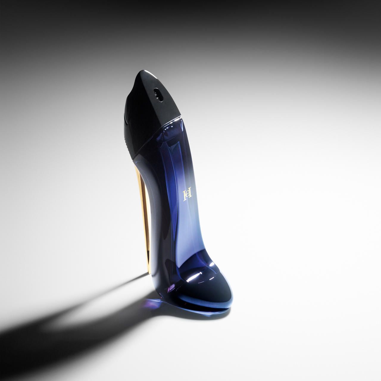 Flacone nero a forma di scarpa con tacco dorato. Liquido blu visibile. Su sfondo bianco.