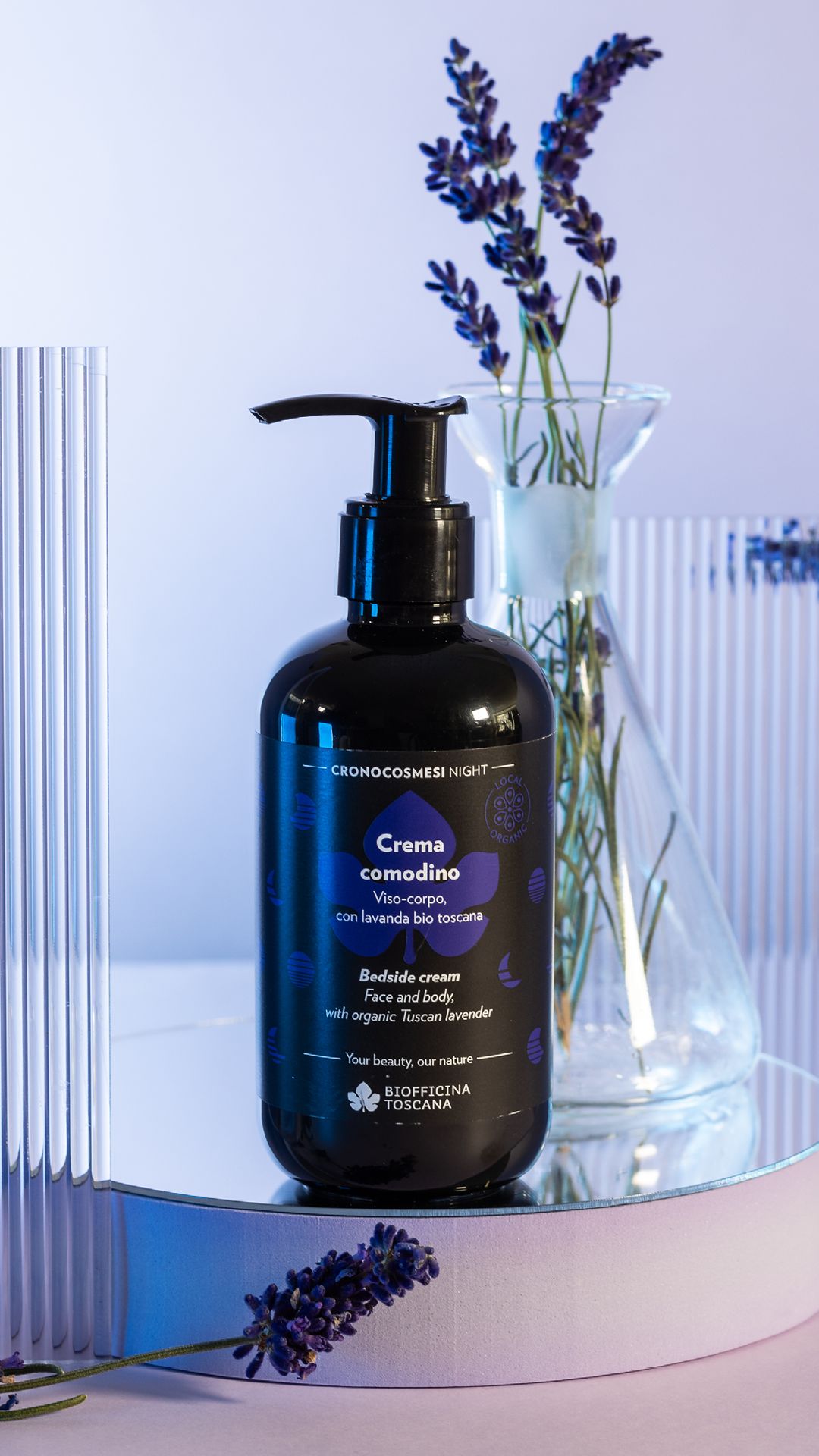 Flacone nero con dosatore su specchio. Rami di lavanda sullo sfondo. Scritta: Crema comodino. Marchio: Biofficina Toscana.