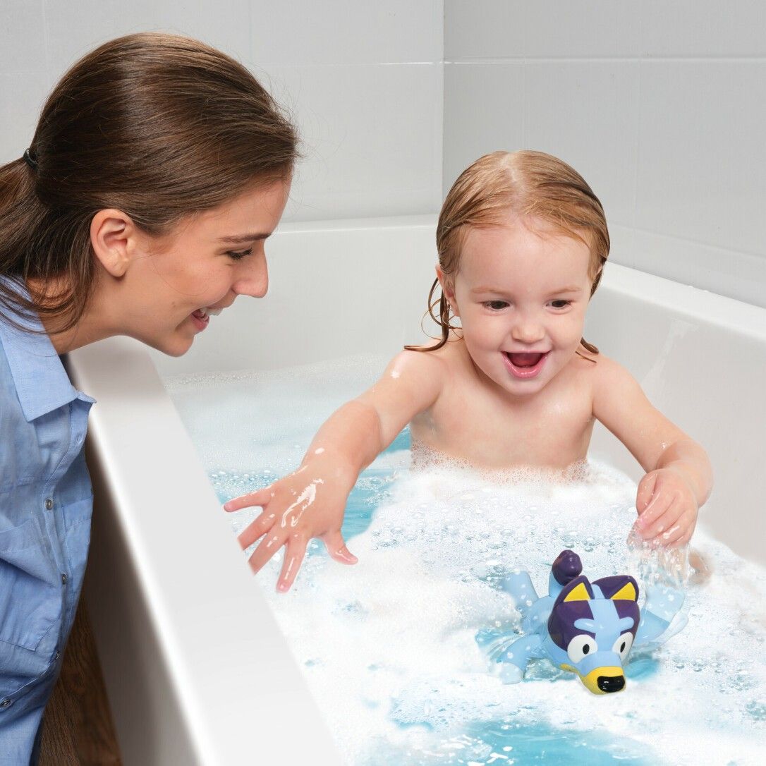 Bambino e donna giocano con il giocattolo da bagno Bluey in una vasca. Acqua e schiuma visibili.