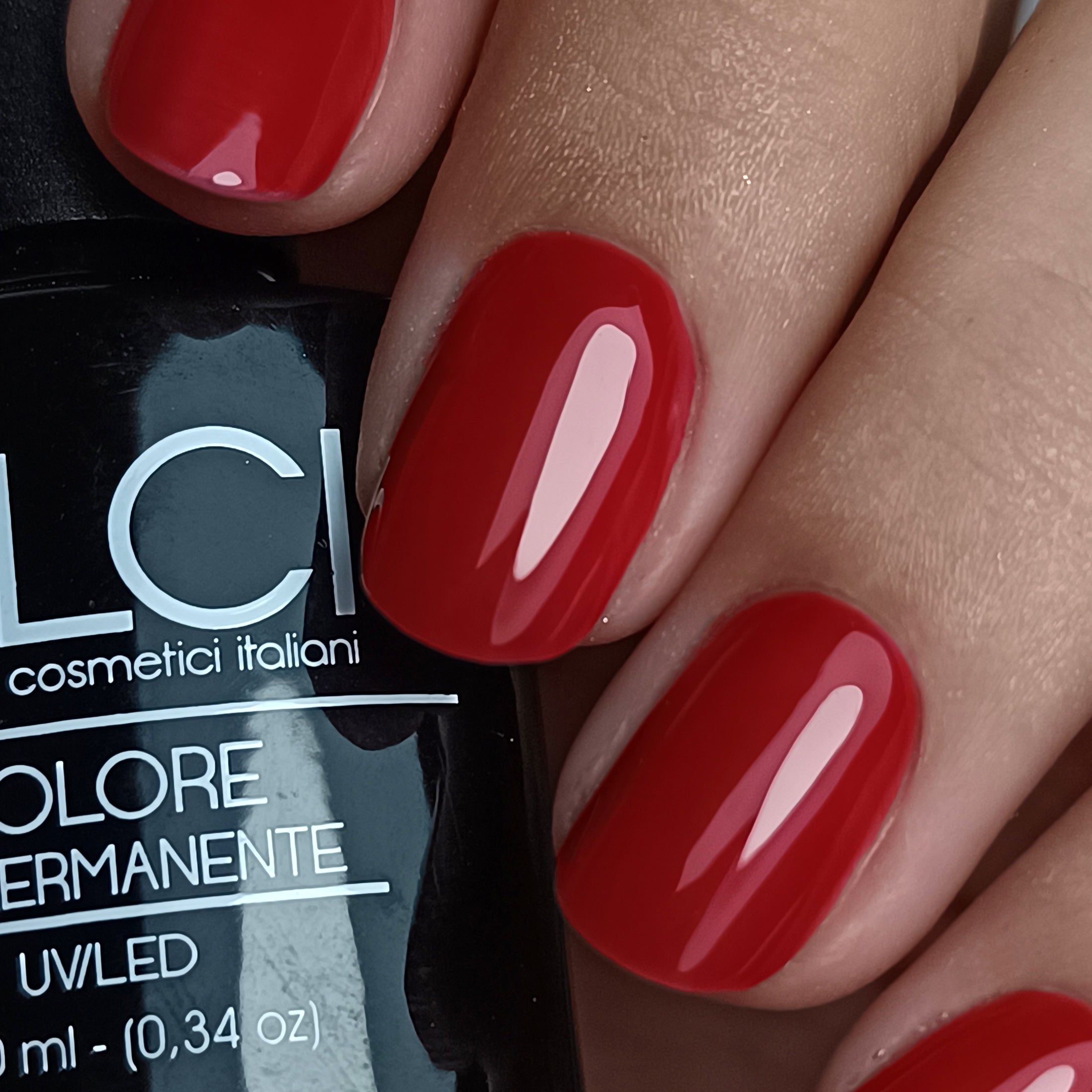 Primo piano di unghie rosse smaltate. Flacone con scritta LCI, Colore Semipermanente, UV/LED.