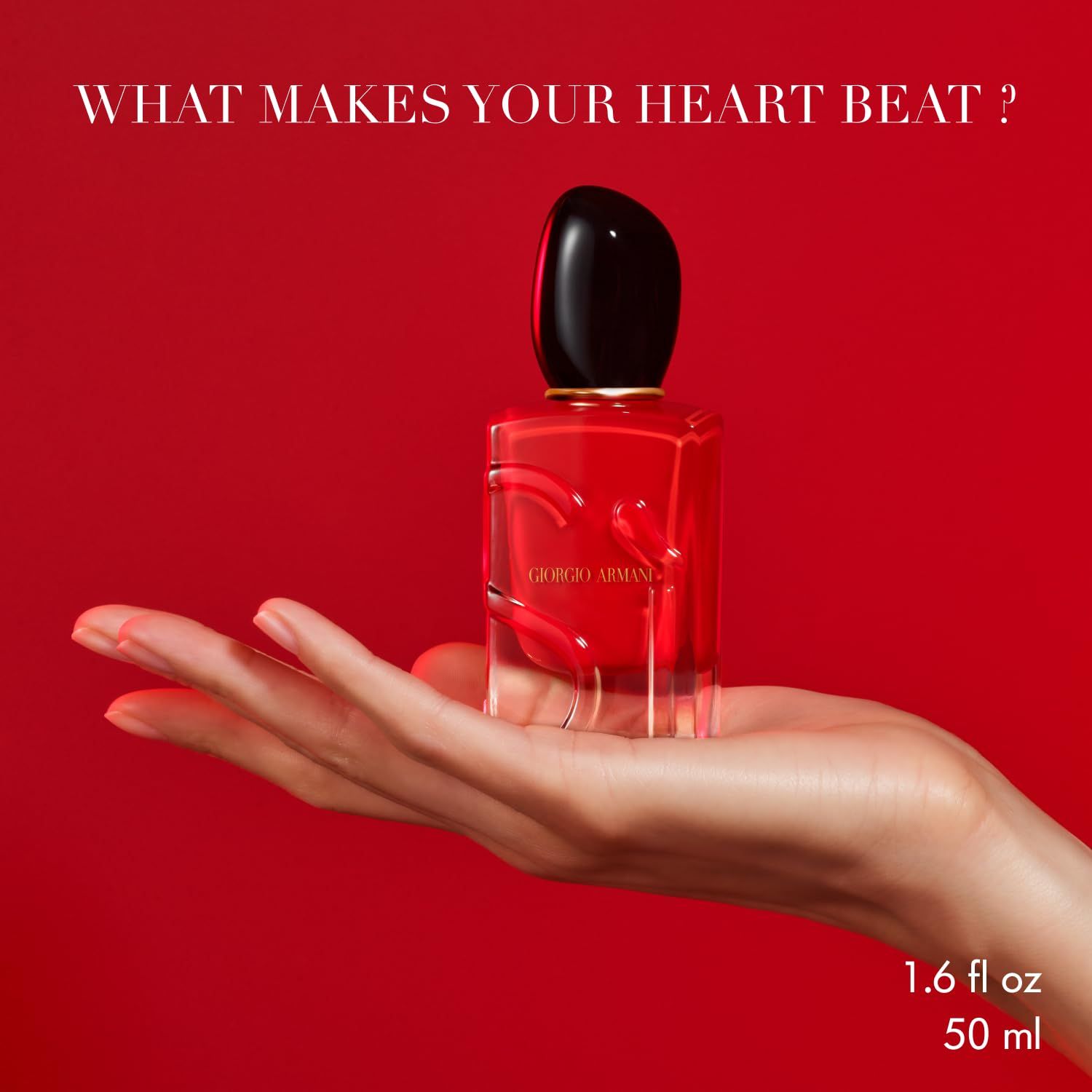 Flacone rosso in una mano. Tappo nero. Scritta: Giorgio Armani. Testo: 1.6 fl oz 50 ml.