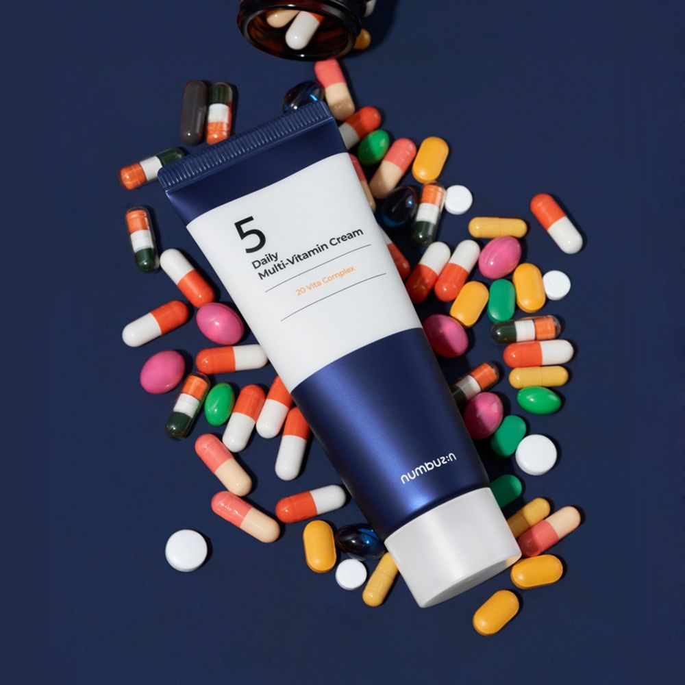 Tubo di crema circondato da pillole colorate. Scritta: 5, Daily Multi-Vitamin Cream, 20 Vita Complex. Marchio: numbuz:n.