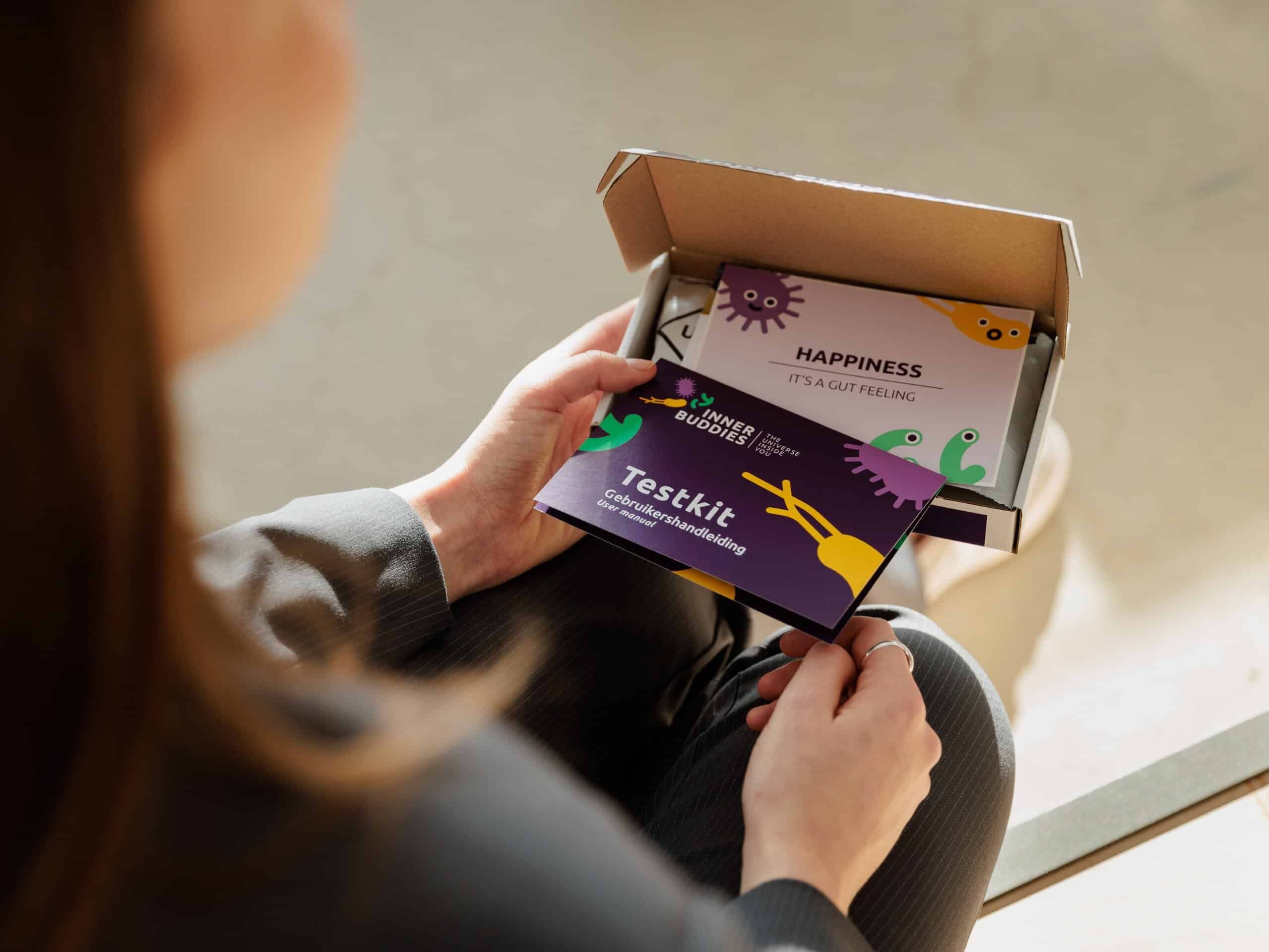Persona che tiene una carta del kit di test Inner Buddies con scritto 'Testkit Raccomandazione Microbioma'.