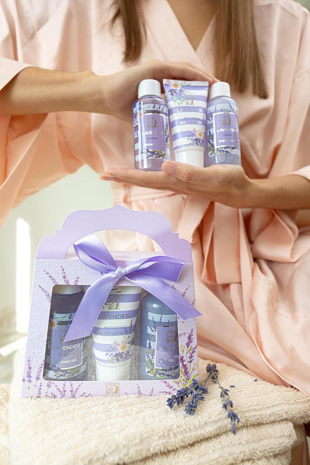 Persona che tiene in mano una confezione regalo con gel doccia, lozione per il corpo e bagno schiuma. Design lavanda. Rami di lavanda accanto.
