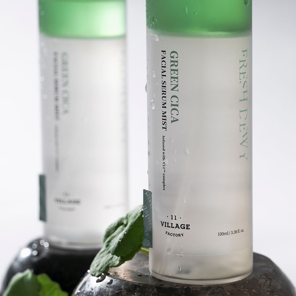 Due flaconi di siero per il viso con accenti verdi. Scritta: Green Cica Facial Serum Mist. Posizionato su una pietra.