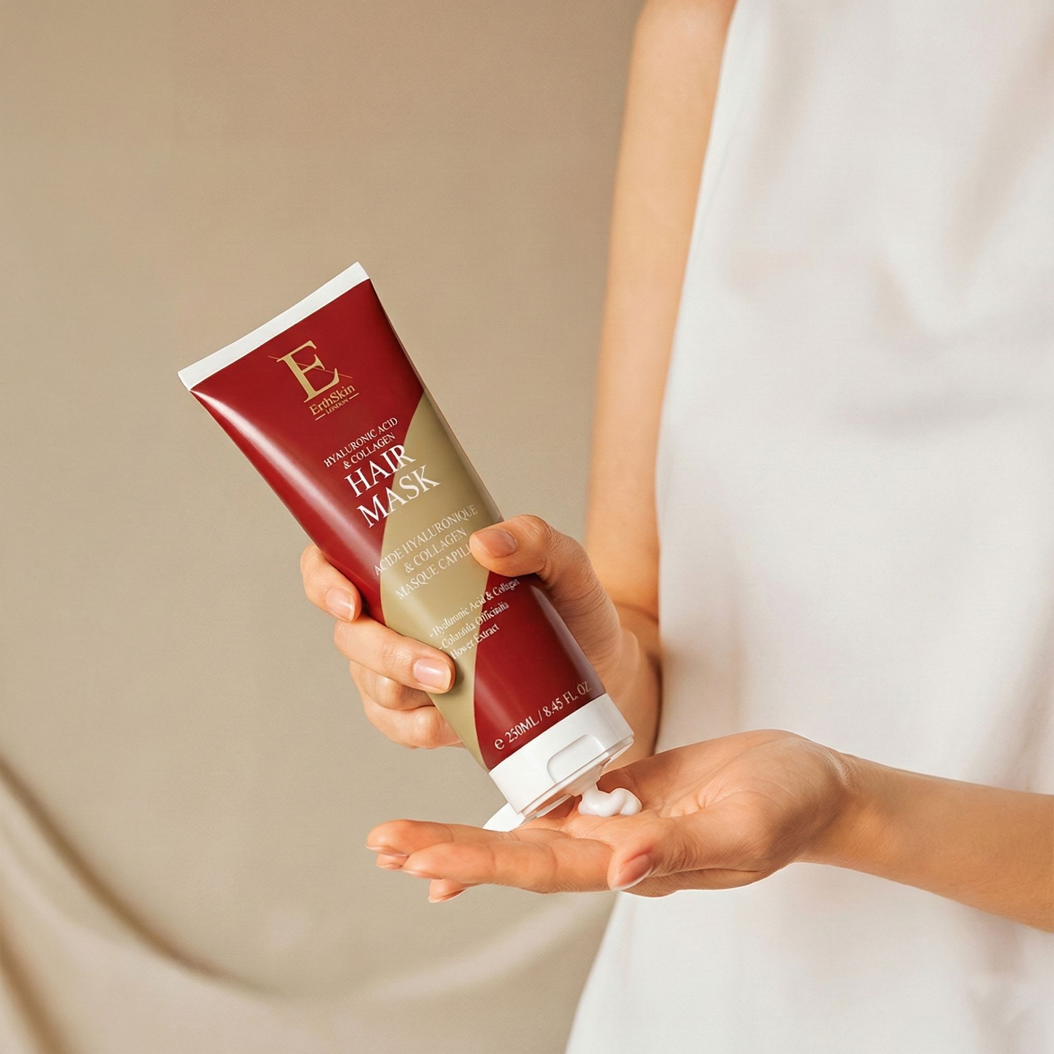 Una mano tiene un tubetto rosso di maschera per capelli all'acido ialuronico e collagene. Viene erogata della crema.