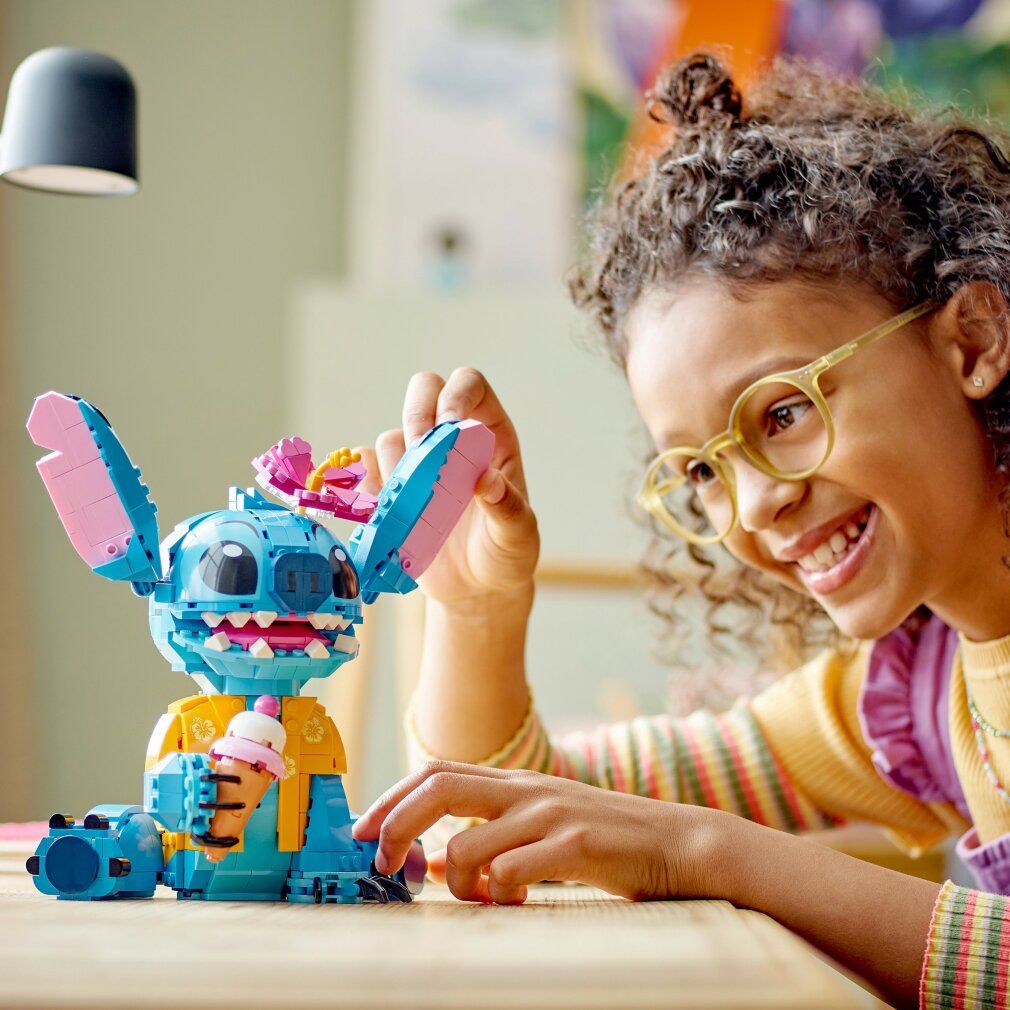 LEGO Stitch blu con orecchie rosa e fiore. Bambina con occhiali guarda Stitch.