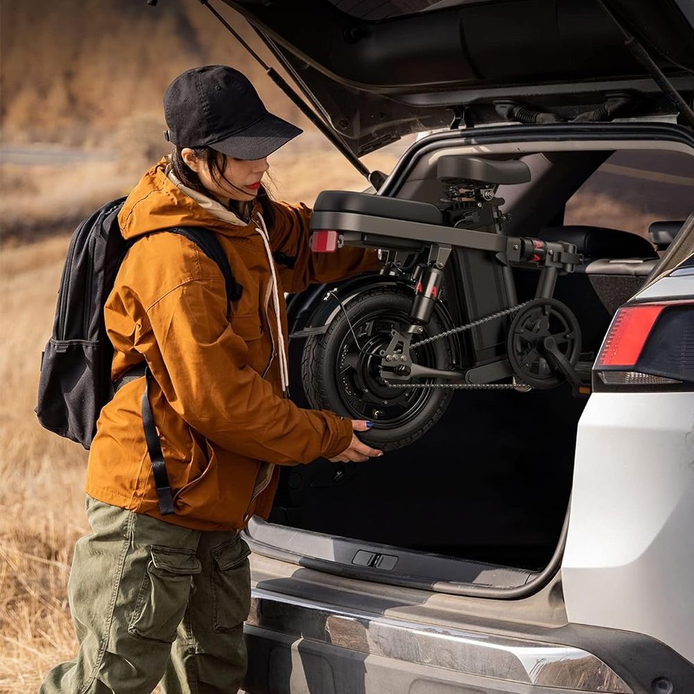 Donna che estrae una e-bike piegata da un bagagliaio. Bicicletta nera.
