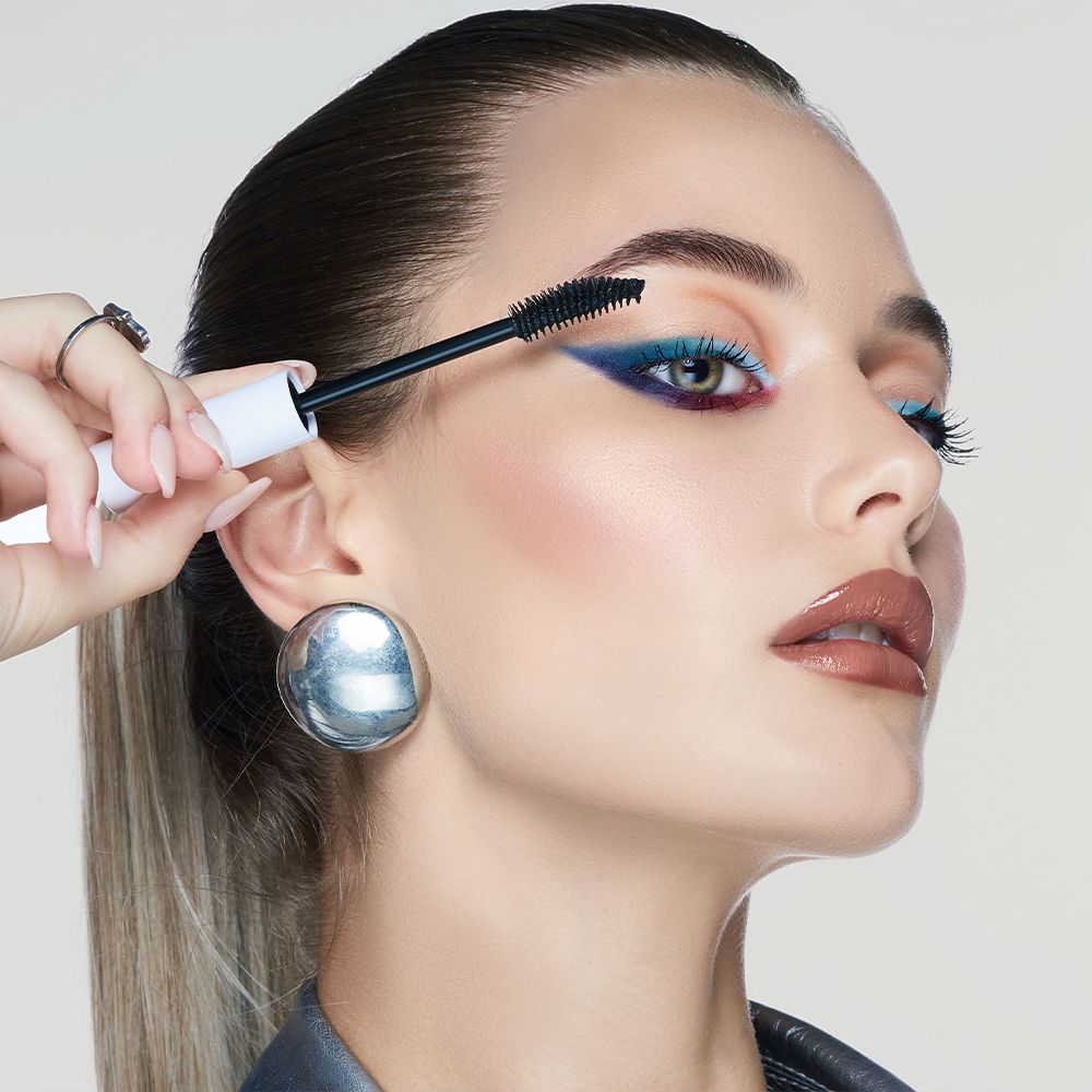 Donna che applica il mascara. Spazzola per mascara nera. Viso truccato. Nome prodotto: Mia Makeup Reset.