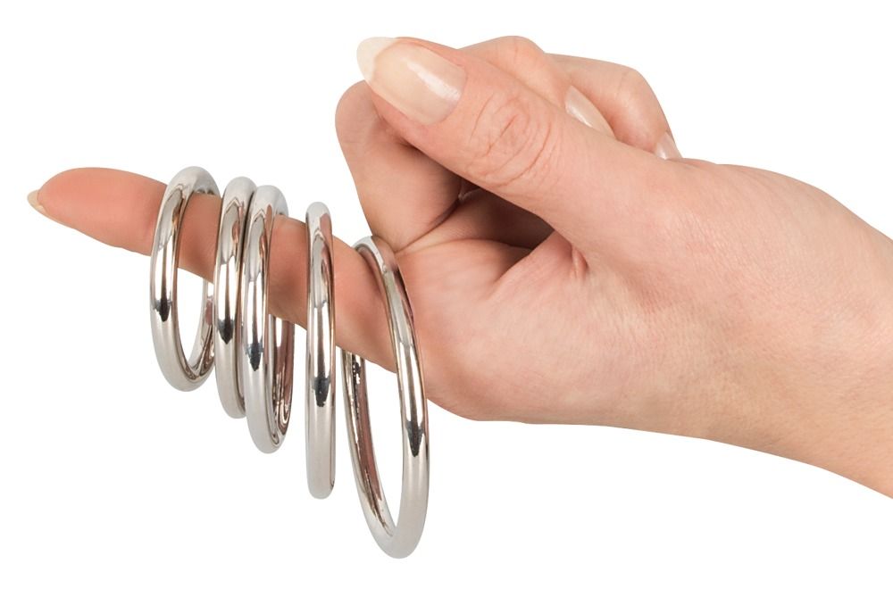 Mano con cinque anelli metallici per pene su un dito. Anelli in metallo lucido.