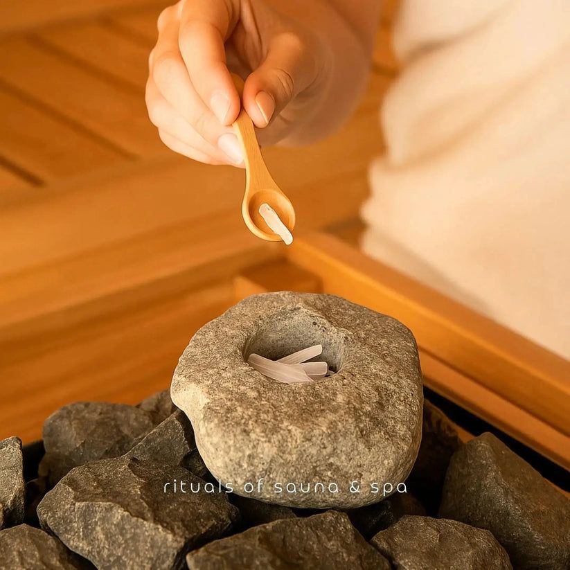 Mano che tiene un cucchiaio di legno con cristalli sopra una pietra con cristalli. Scritta: rituals of sauna & spa.