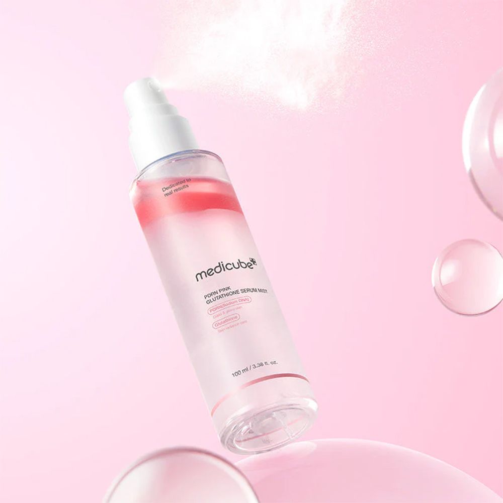 Flacone spray Medicube PDRN Pink Glutathione Serum Mist che spruzza nebbia. Sfere di vetro fluttuanti e sfondo rosa.