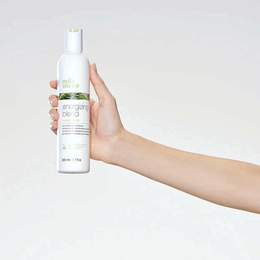 Flacone bianco Milk_shake Energizing Blend Conditioner, tenuto in mano. Tappo verde ed etichetta con informazioni sul prodotto.