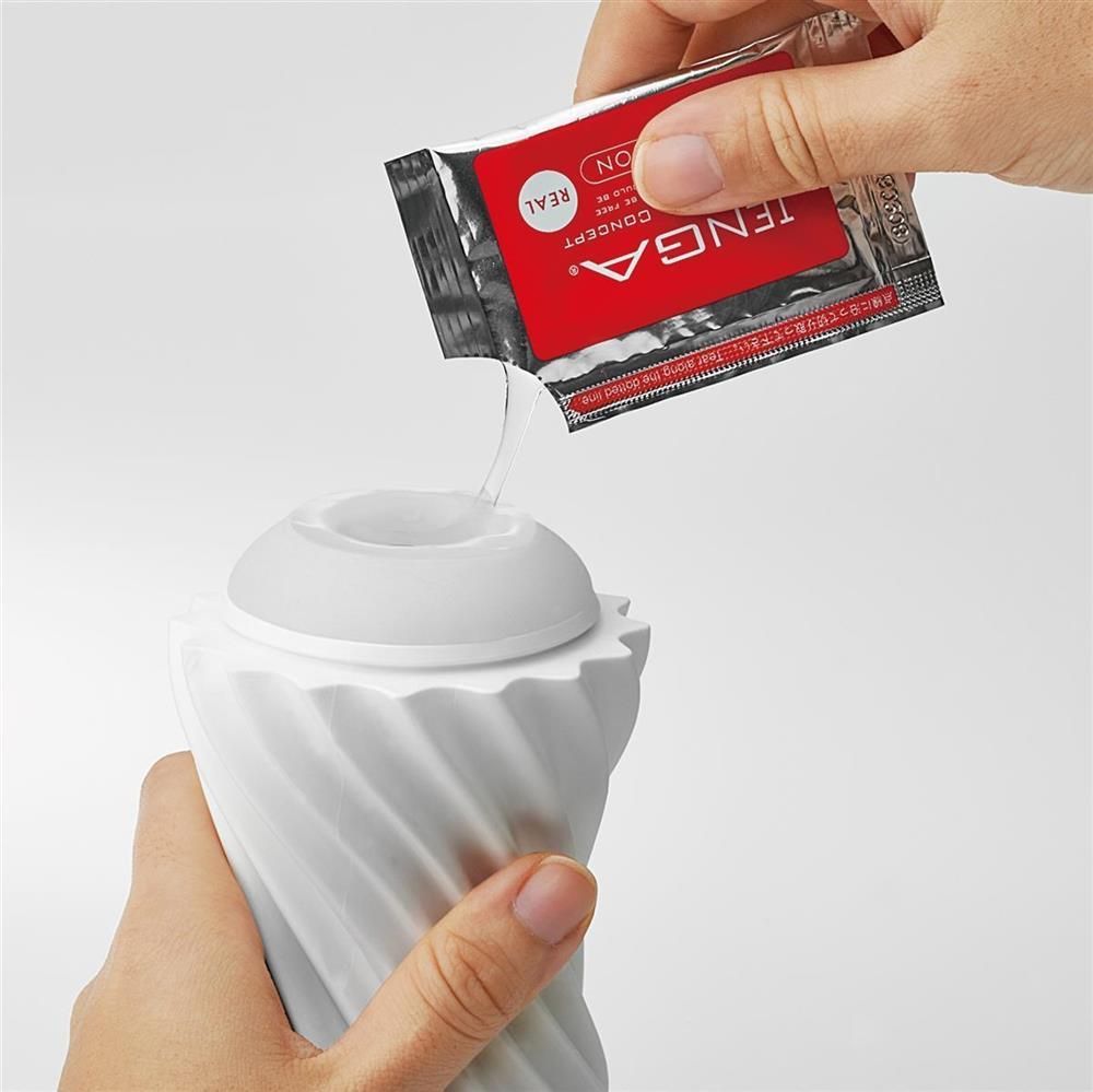 Mano che versa lubrificante da una confezione TENGA in un prodotto bianco. Prodotto con superficie scanalata.