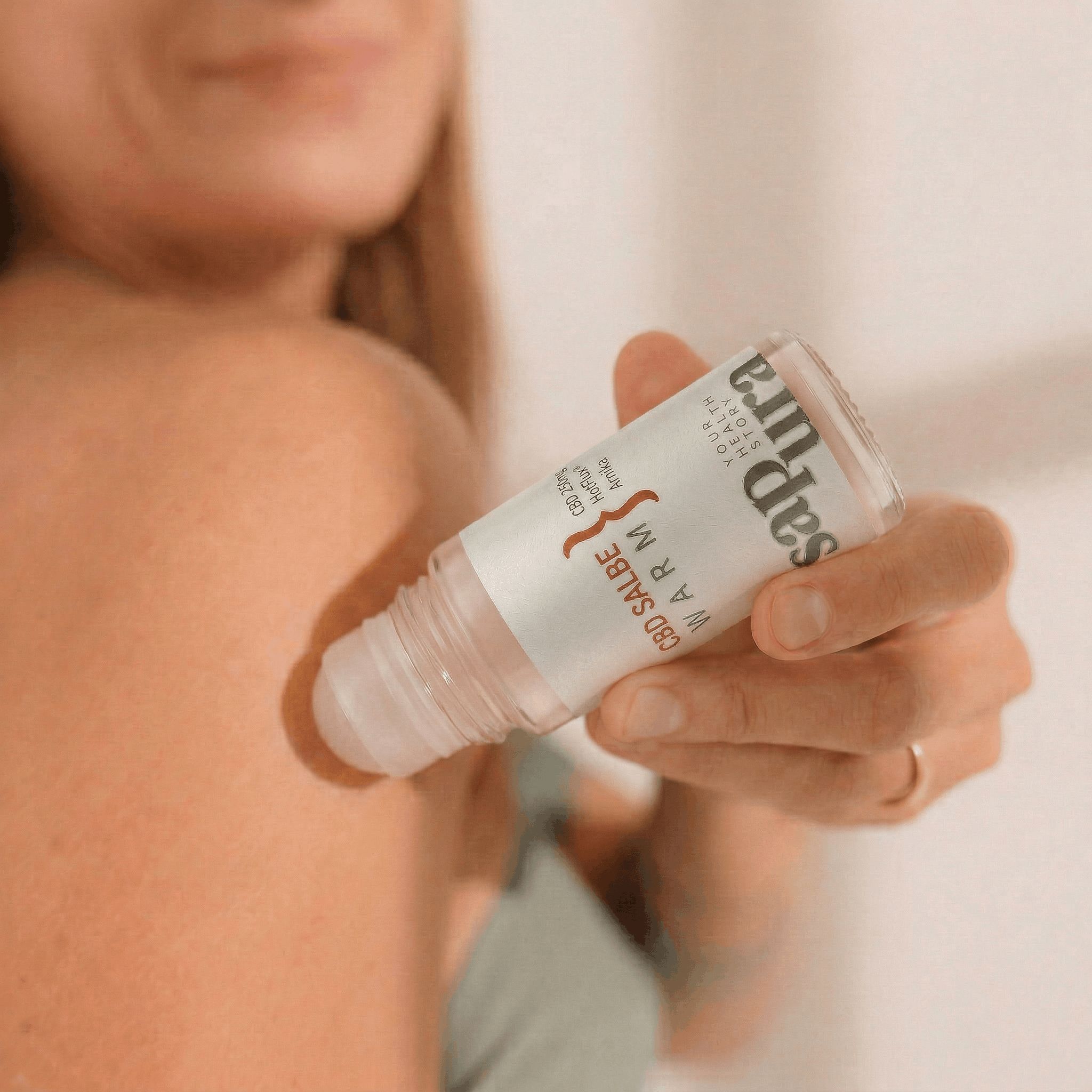 Mano che tiene un flacone roll-on balsamo CBD Caldo sulla schiena di una persona. L'applicatore è rivolto verso la pelle.