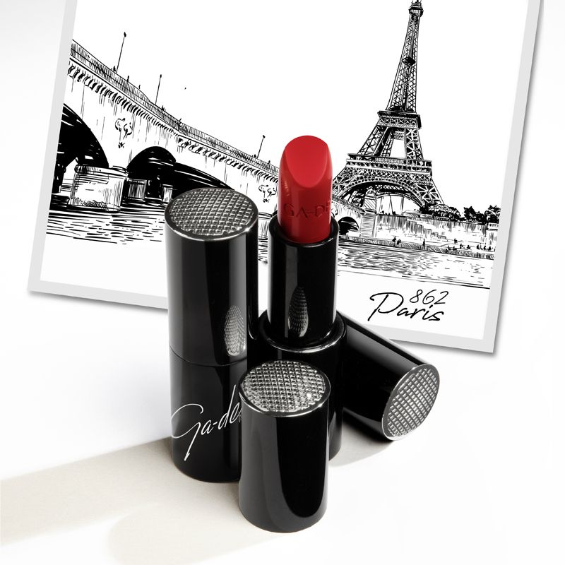 Rossetto rosso aperto. Astucci neri con cappucci argentati. Logo Ga-De. Sfondo: illustrazione di Parigi.