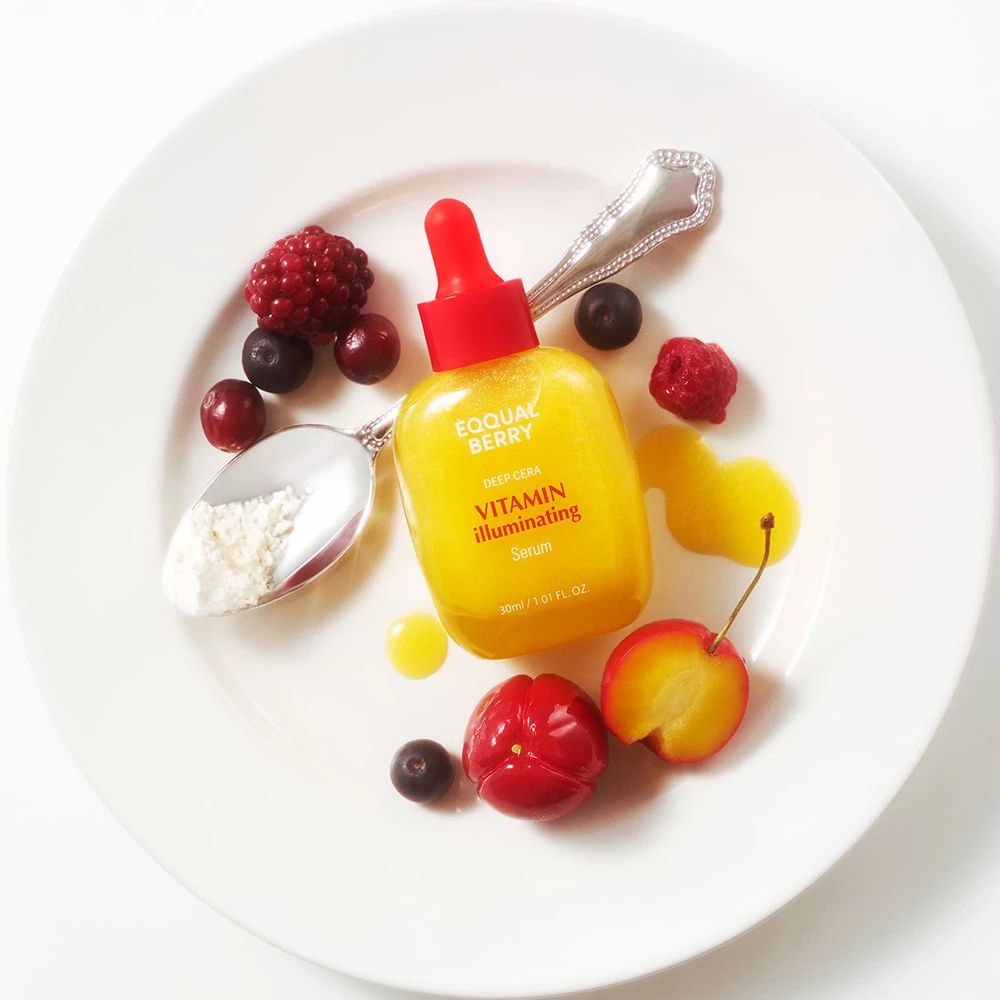 Flacone di siero giallo su un piatto con frutta e cucchiaio. Scritta: EQQUAL BERRY, Vitamin Illuminating Serum.