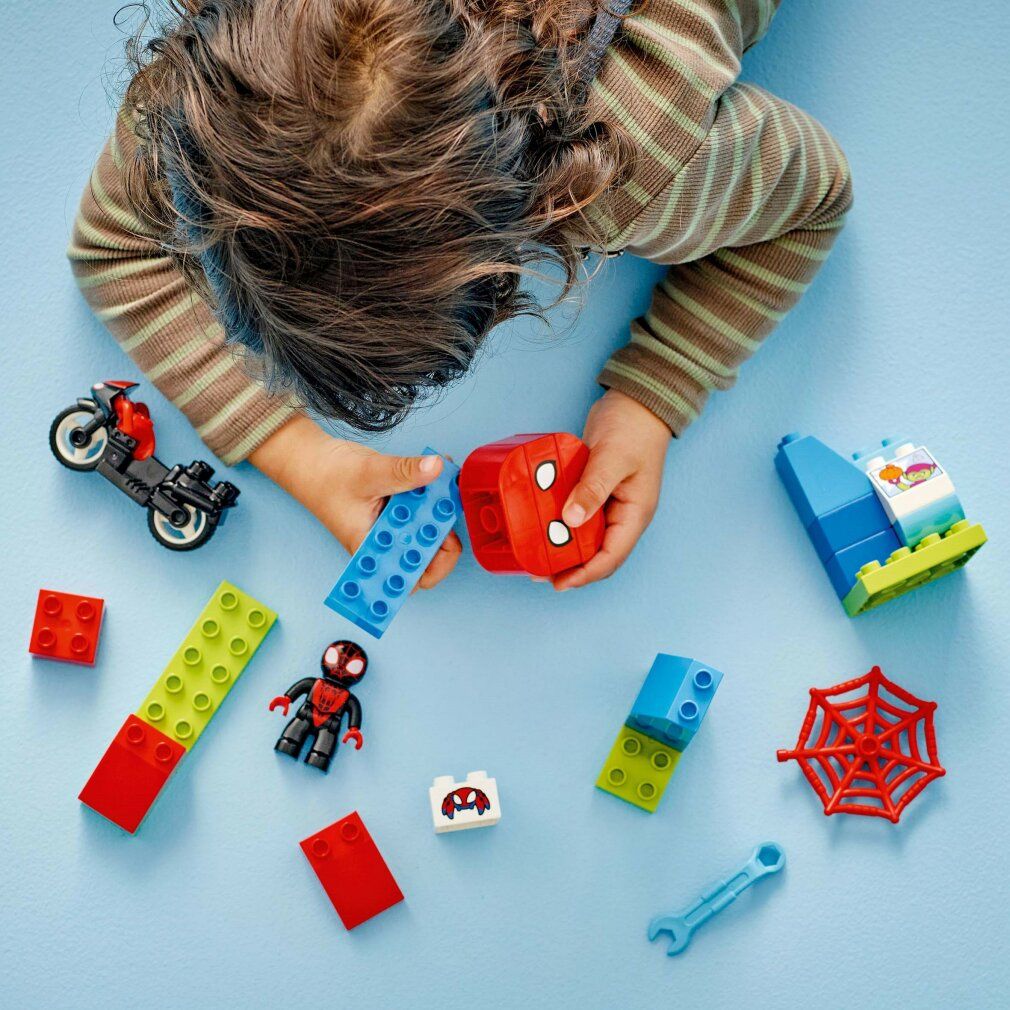 Set LEGO Duplo. Moto, personaggio, edificio, ragnatela, attrezzo. Pezzi su sfondo blu, vista dall'alto.