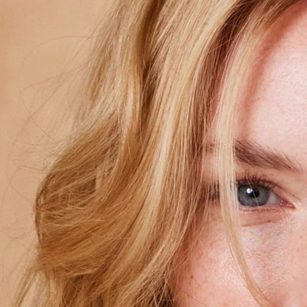 Primo piano di un viso con capelli biondi e un occhio blu. I capelli cadono sulla fronte. Pelle con lentiggini.