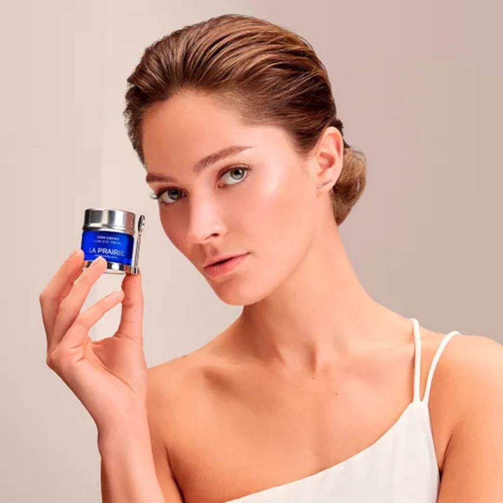 Donna tiene in mano un vasetto blu con coperchio argentato. Scritta: Skin Caviar Luxe Eye Cream, La Prairie, Svizzera.