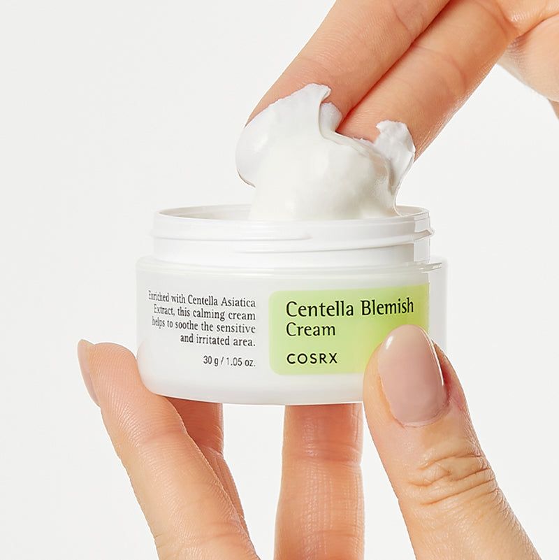 Mano con vasetto e crema sul dito. Scritta: Centella Blemish Cream, COSRX. Etichetta verde e bianca. Testo: 30 g / 1,05 OZ.