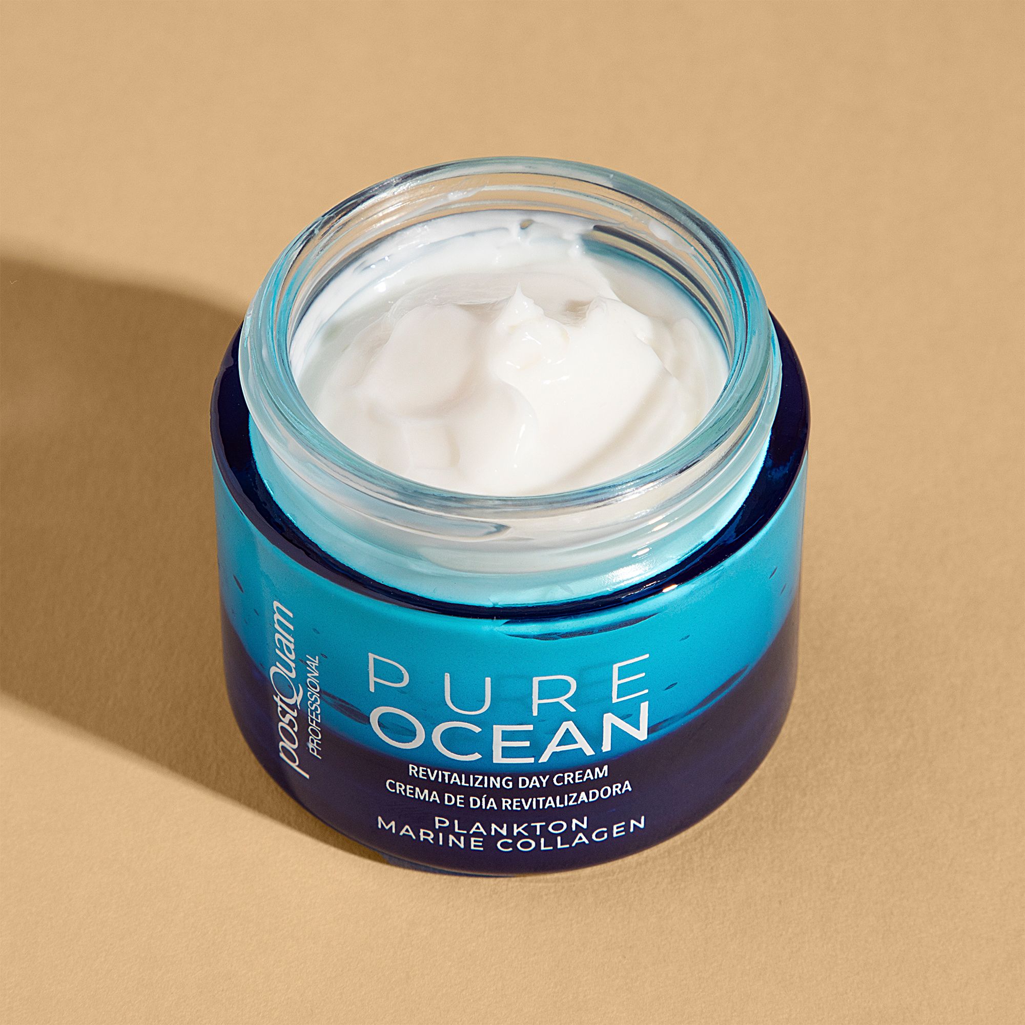 Vasetto di crema blu aperto con crema bianca. Scritta: PURE OCEAN, Revitalizing Day Cream, Plankton Marine Collagen. Marchio: Postquam.