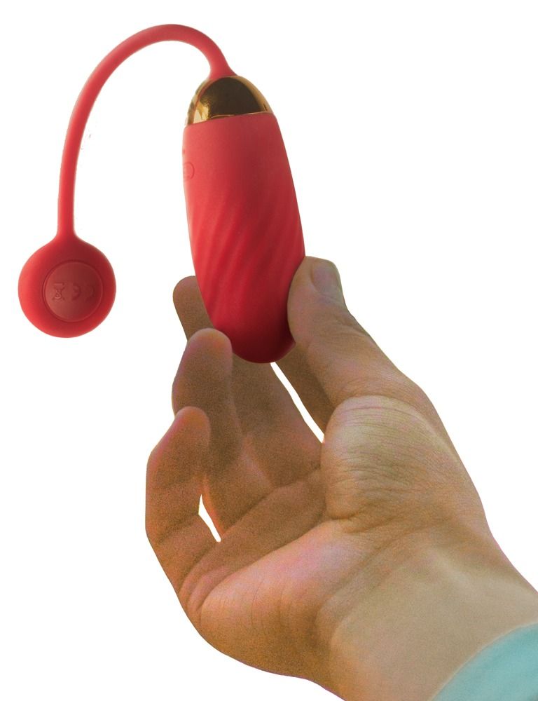 Vibratore rosso con finitura dorata, tenuto in mano. Base rotonda rossa visibile.