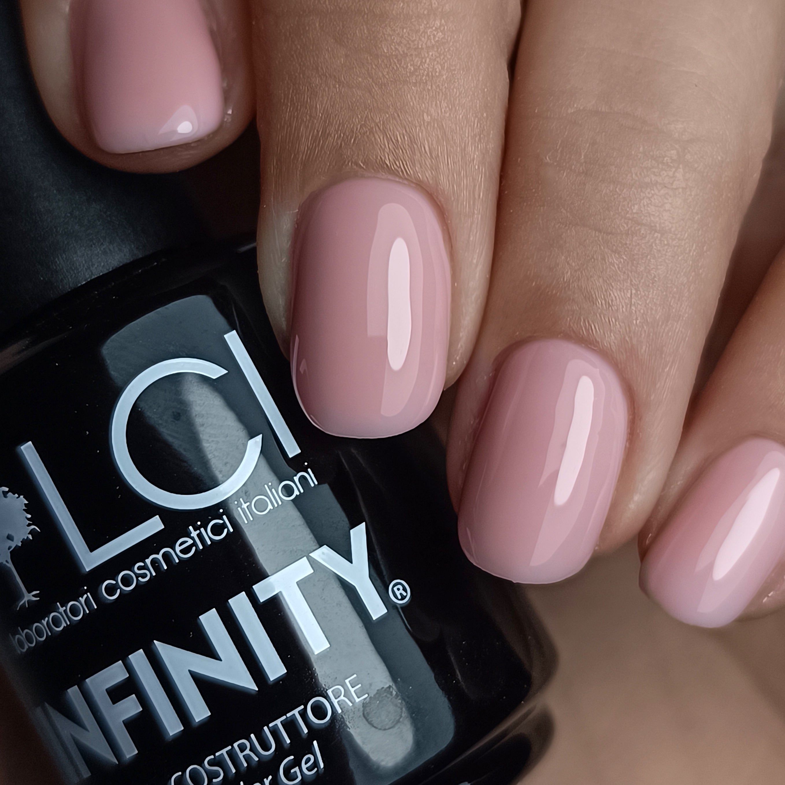 Mano con unghie smaltate nude-rosa. Flacone con scritta LCI INFINITY.