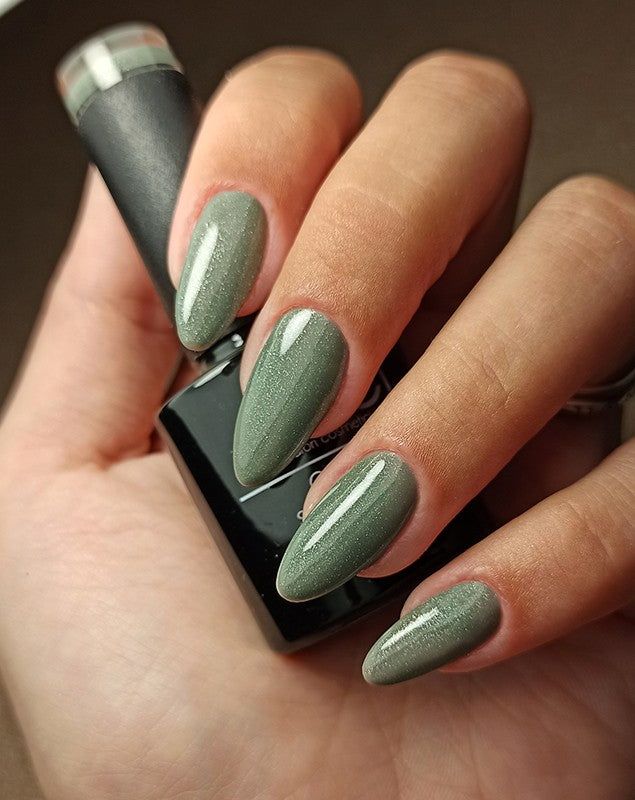 Mano con unghie smaltate verde glitterato. Flacone di smalto sullo sfondo.