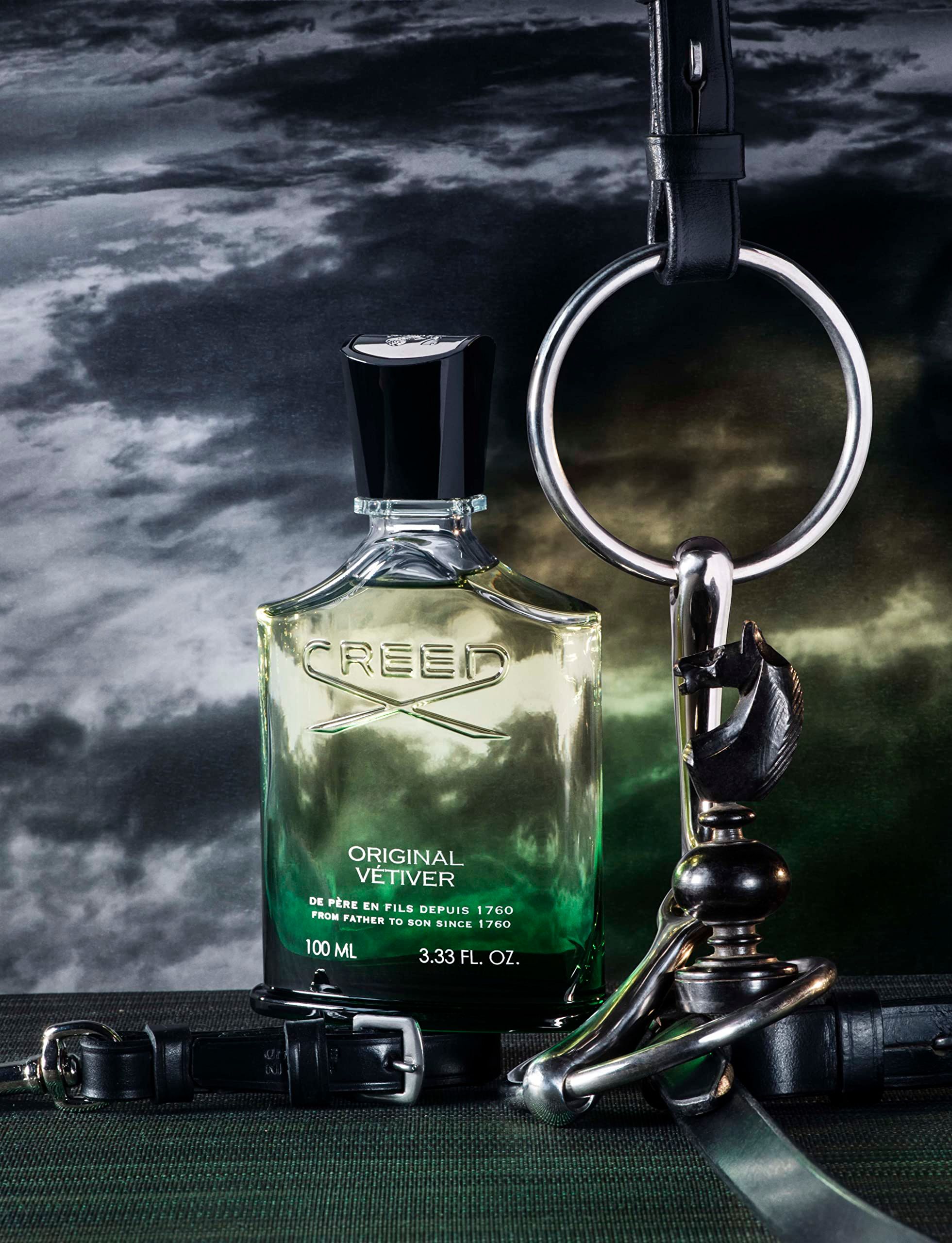 Flacone di profumo in vetro verde con tappo nero. Scritta: CREED ORIGINAL VETIVER. 100 ML. Con accessori in pelle.