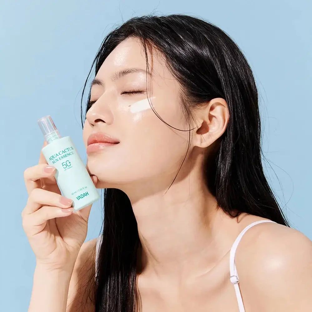 Donna con occhi chiusi tiene in mano un flacone. Prodotto applicato sulla pelle. Flacone con scritta YADAH Aqua Cactus Sun.