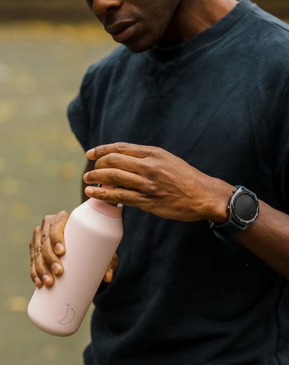 Persona tiene borraccia rosa, apre il tappo. Maglietta nera, orologio al polso.