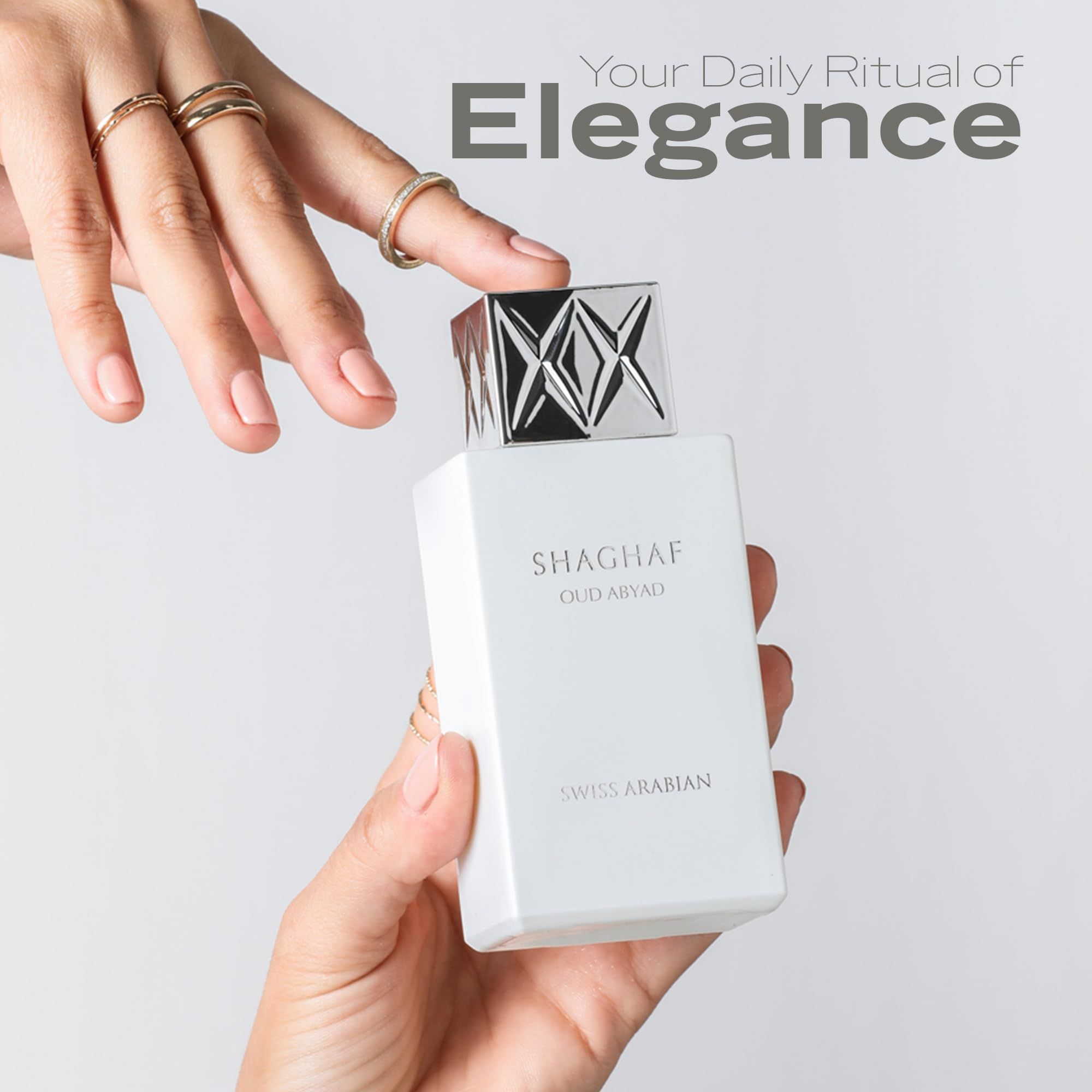 Mani che tengono flacone bianco con tappo argento. Testo: SHAGHAF OUD ABYAD, SWISS ARABIAN. Primo piano.