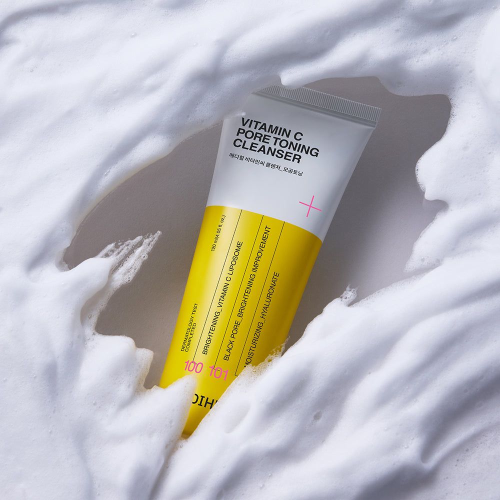 Tubo giallo con schiuma bianca. Scritta: Vitamin C Pore Toning Cleanser. Segno più rosa. Striscia gialla con testo.