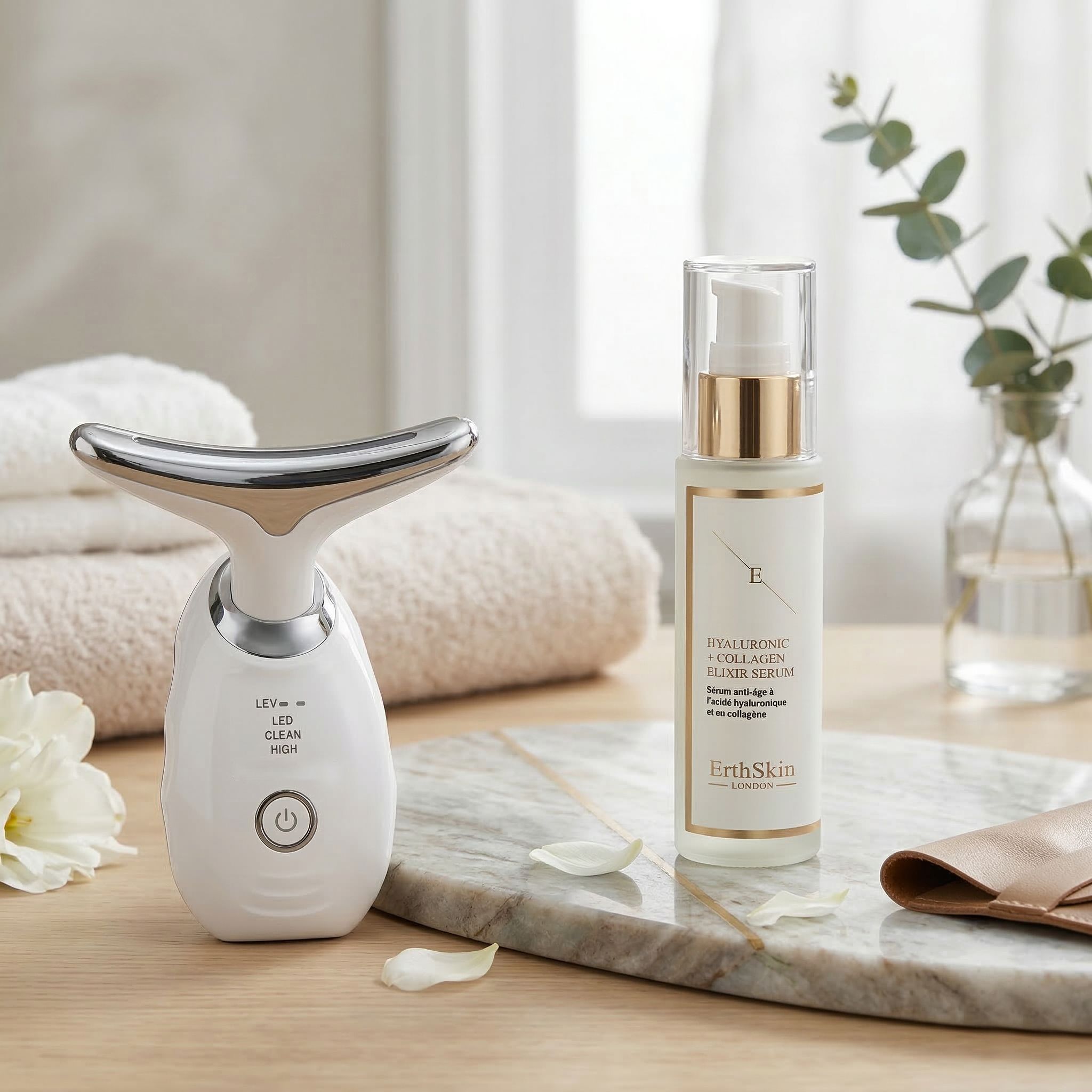 Massaggiatore cervicale LED Erth Skin London e siero elisir acido ialuronico e collagene su lastra di marmo.