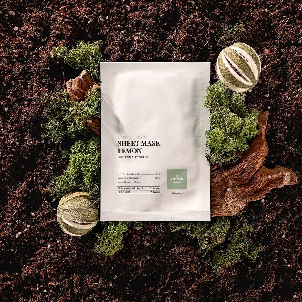 Maschera in tessuto bianca con testo. Circondata da muschio, legno e fette di limone essiccate. Scritta: SHEET MASK LEMON.
