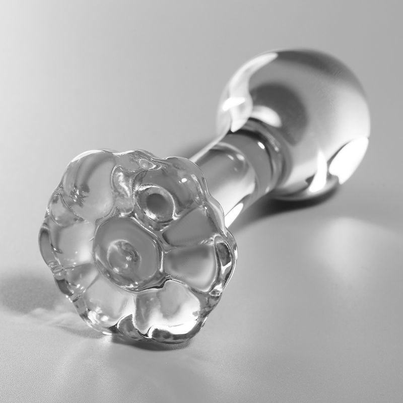 Plug anale in vetro trasparente, sdraiato, con base dettagliata a forma di fiore.