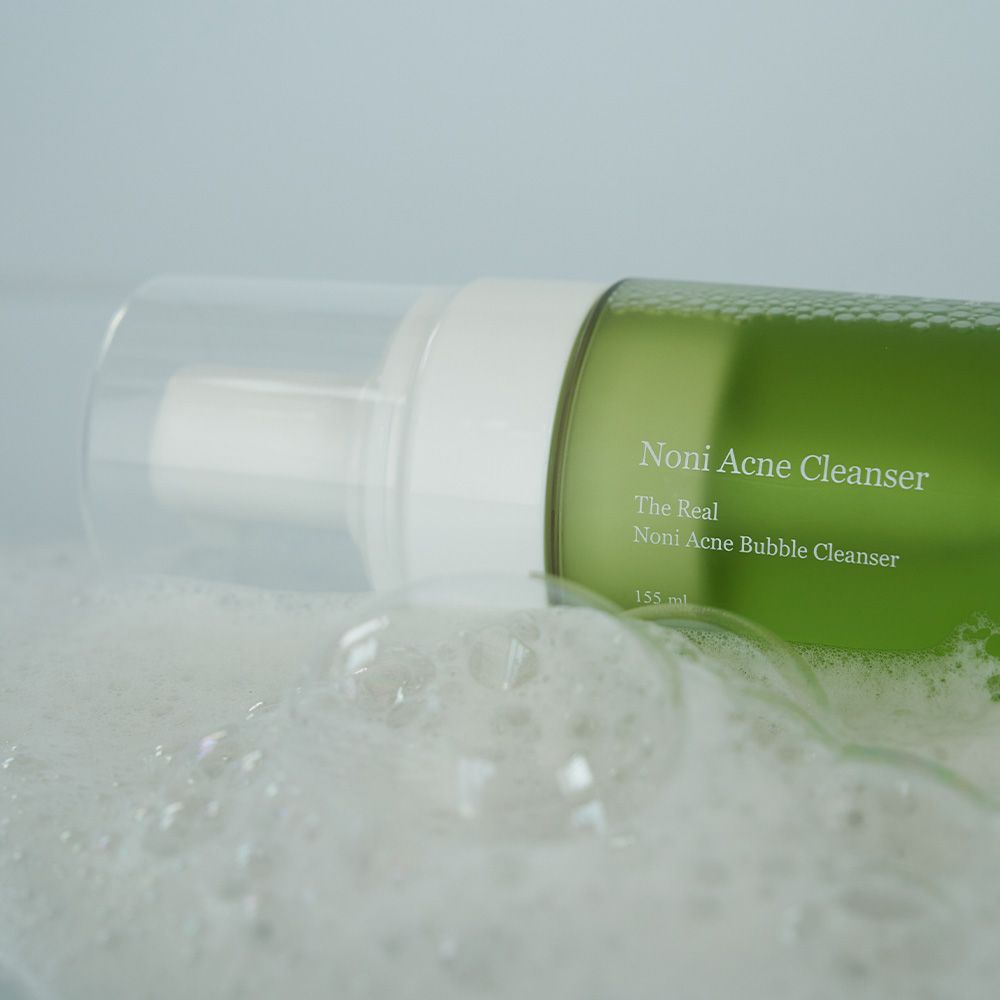 Detergente schiumogeno anti-acne Celimax Noni immerso nella schiuma, con bolle visibili ed etichetta del prodotto.