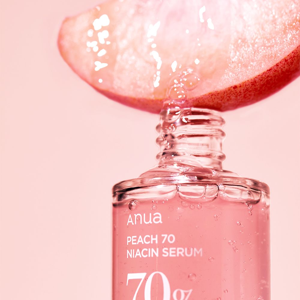 Gocce da una fetta di pesca cadono nel flacone del siero Anua Peach 70 Niacin.