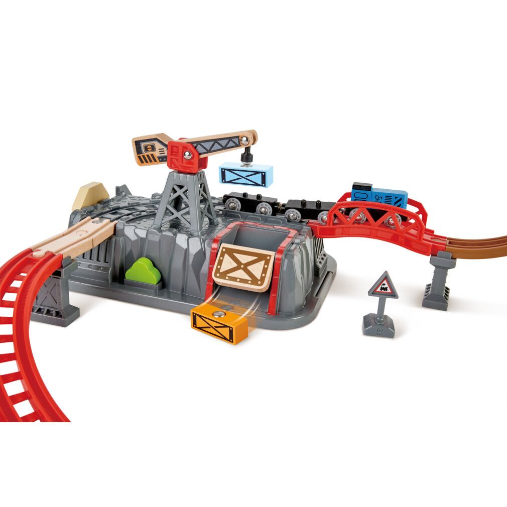 Primo piano del set di costruzioni ferroviarie. Include una base rocciosa grigia, un ponte rosso e una gru. Treni e container visibili.