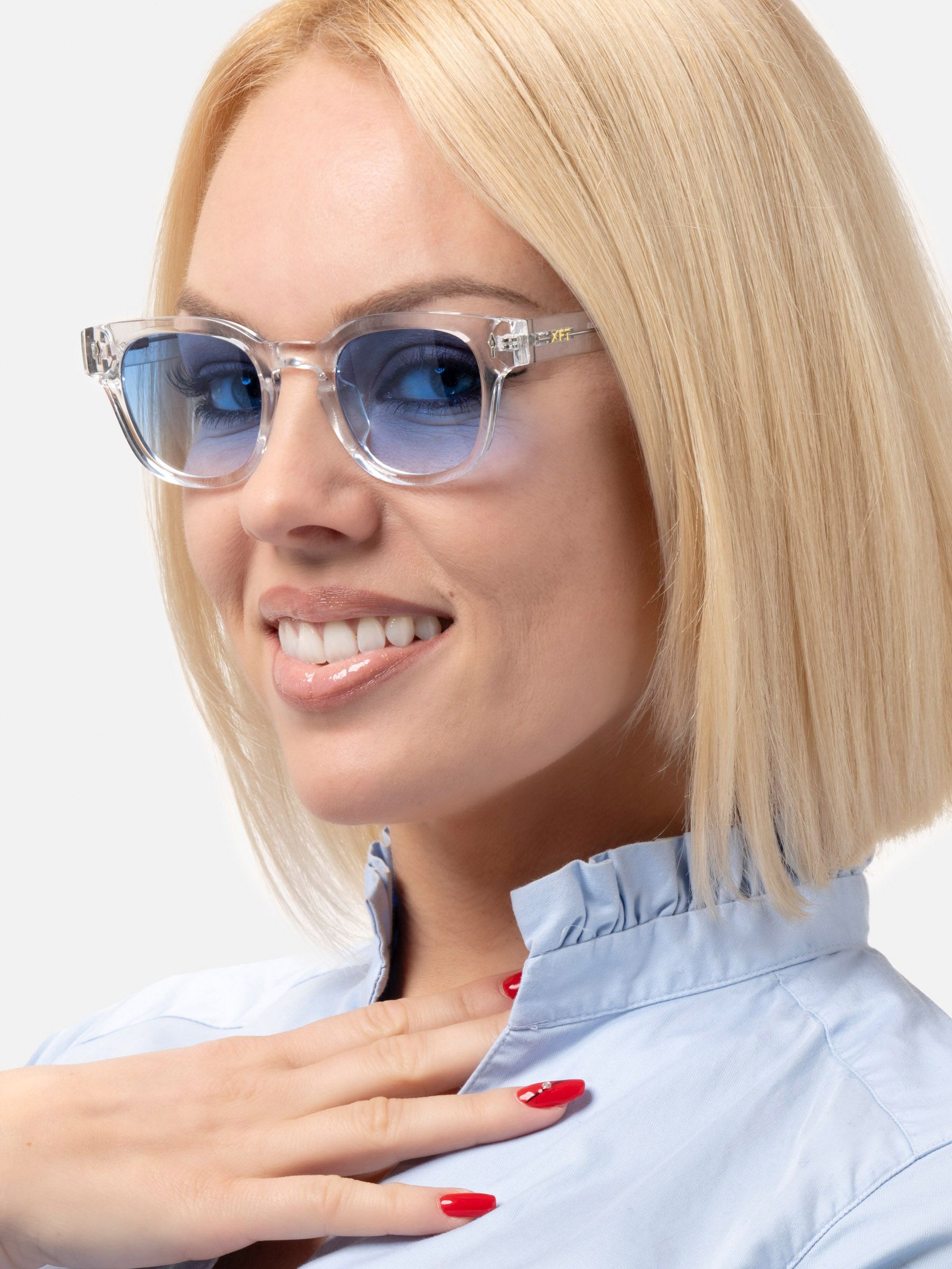 Donna bionda con occhiali da sole trasparenti e lenti blu. Vista laterale, sorridente.