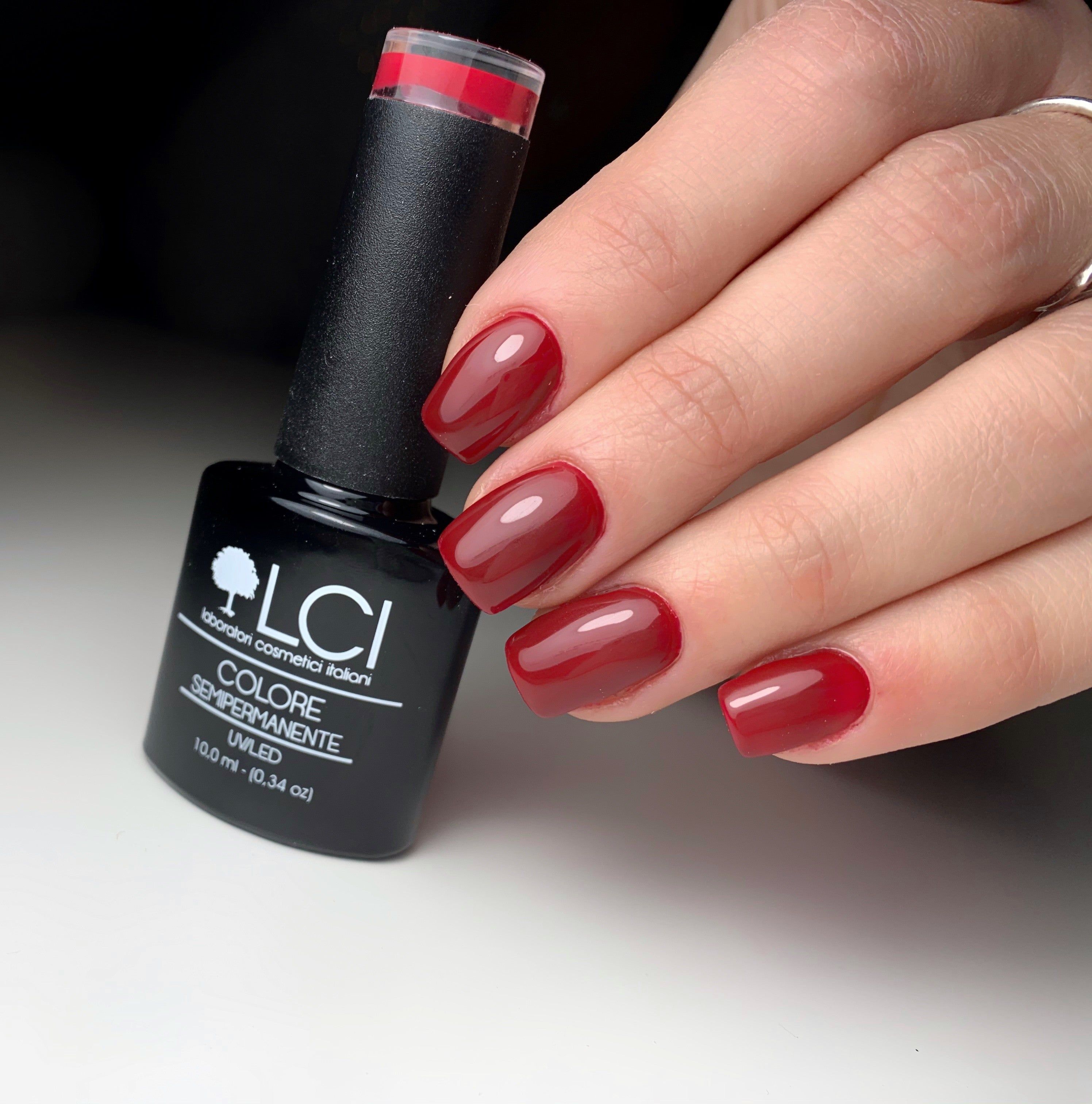 Unghie rosse e flacone di smalto. Scritta: LCI, Colore Semipermanente, UVLED 10,0 ml.