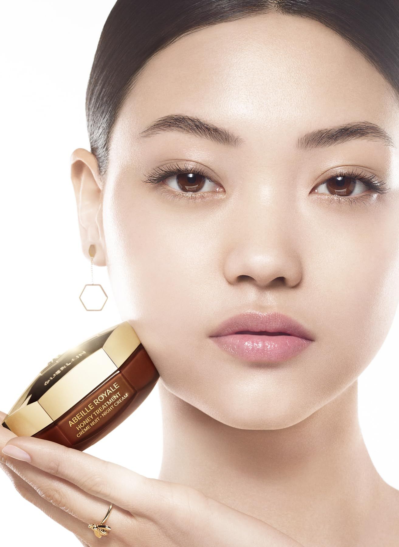 Donna asiatica che tiene un vasetto di crema sulla guancia. Scritta: ABEILLE ROYALE HONEY TREATMENT CRÈME NUIT NIGHT CREAM.
