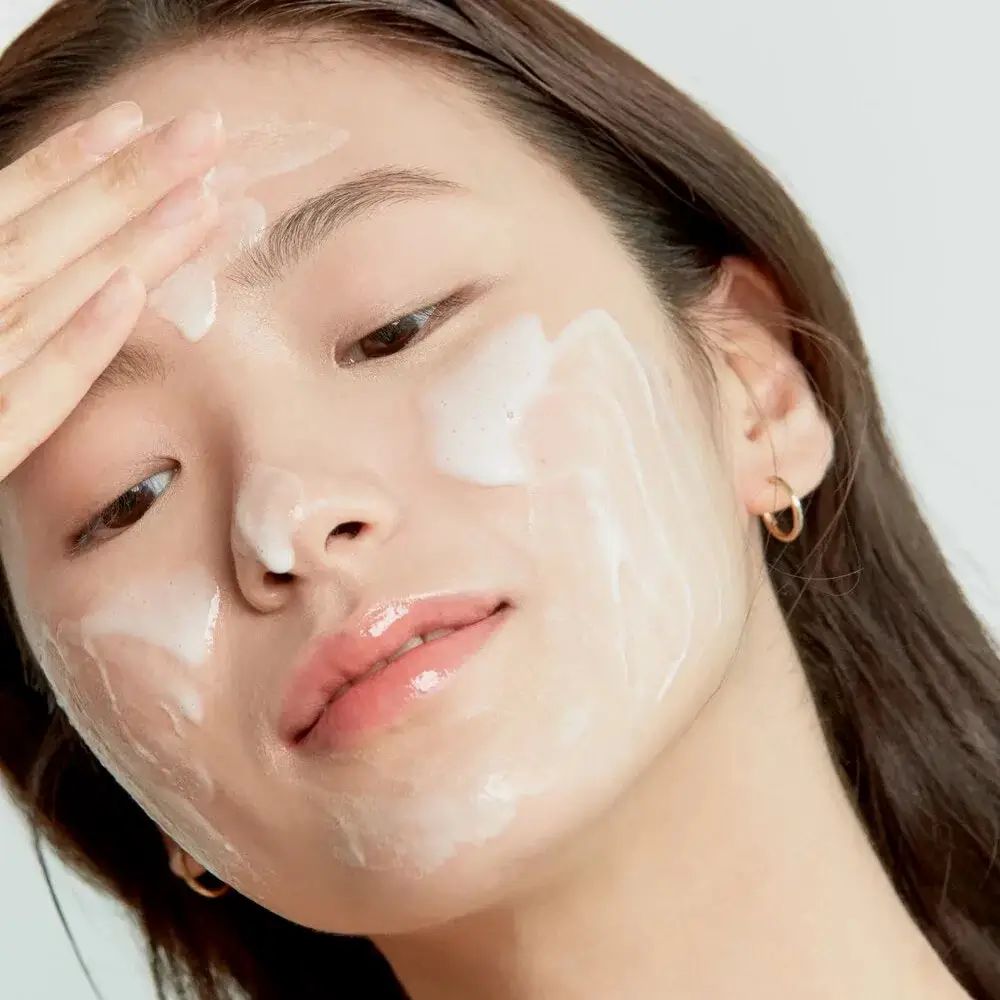 Viso di una persona ricoperto di schiuma. La persona tocca il suo viso. Nessun nome del prodotto visibile.