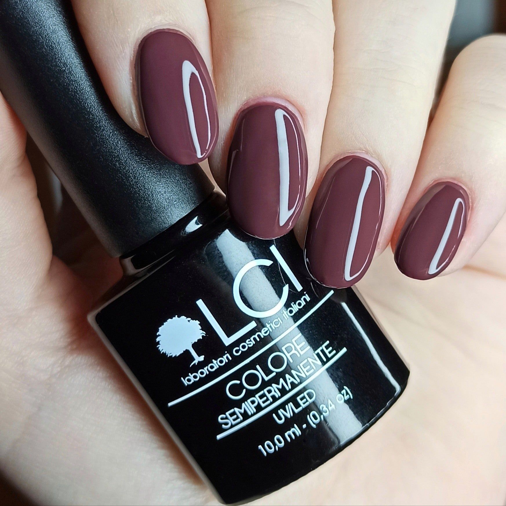Mano con unghie smaltate di viola. Accanto, flacone di smalto con scritta: LCI, Colore Semipermanente, UVLED.