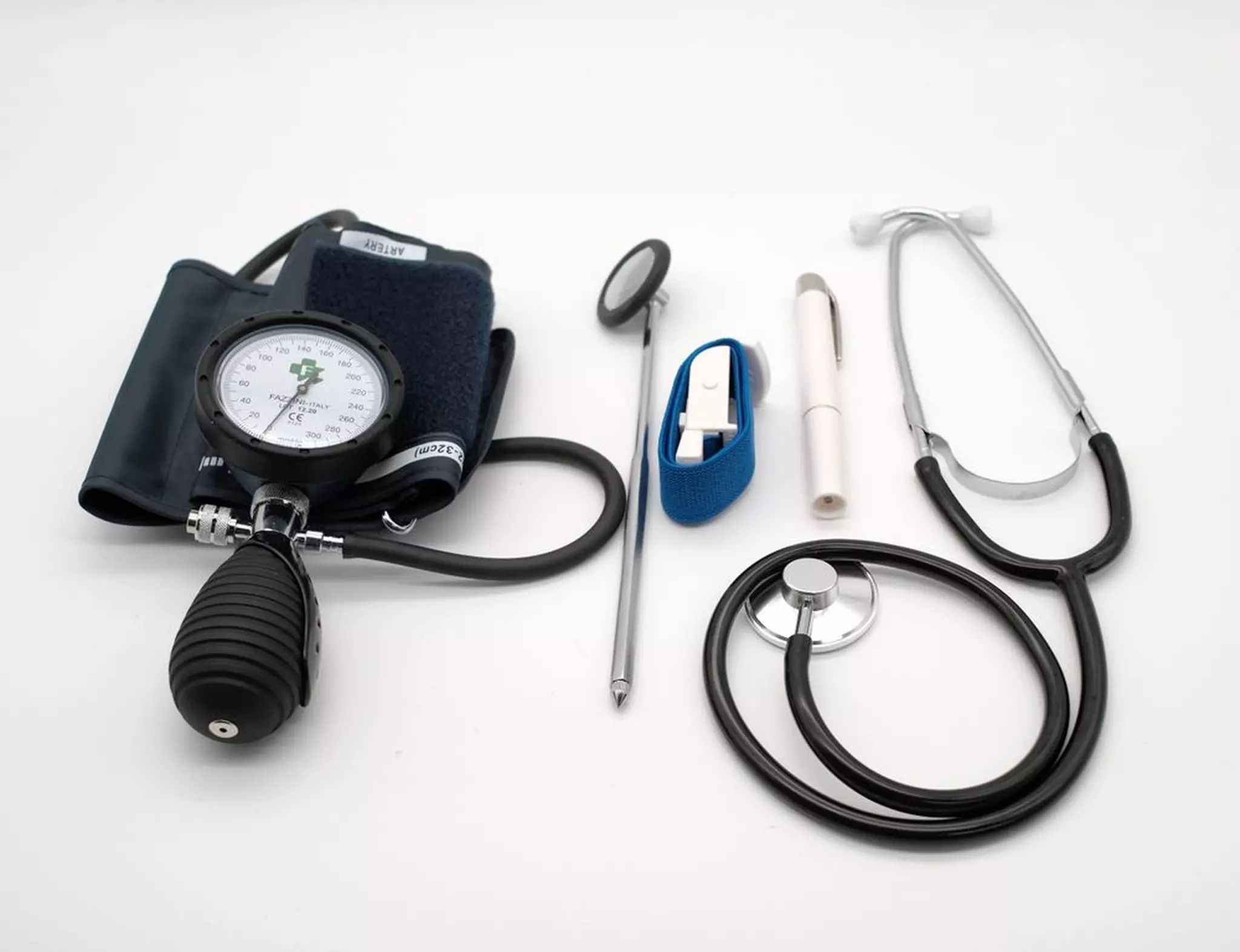 Set medico con stetoscopio, martello per riflessi, torcia pupillare e sfigmomanometro. Su sfondo bianco.