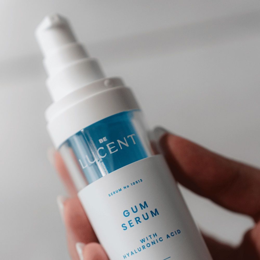 Primo piano di un flacone di siero gengivale. Bianco e blu. Scritta: GUM SERUM, Be Lucent. Con acido ialuronico. Tenuto in mano.