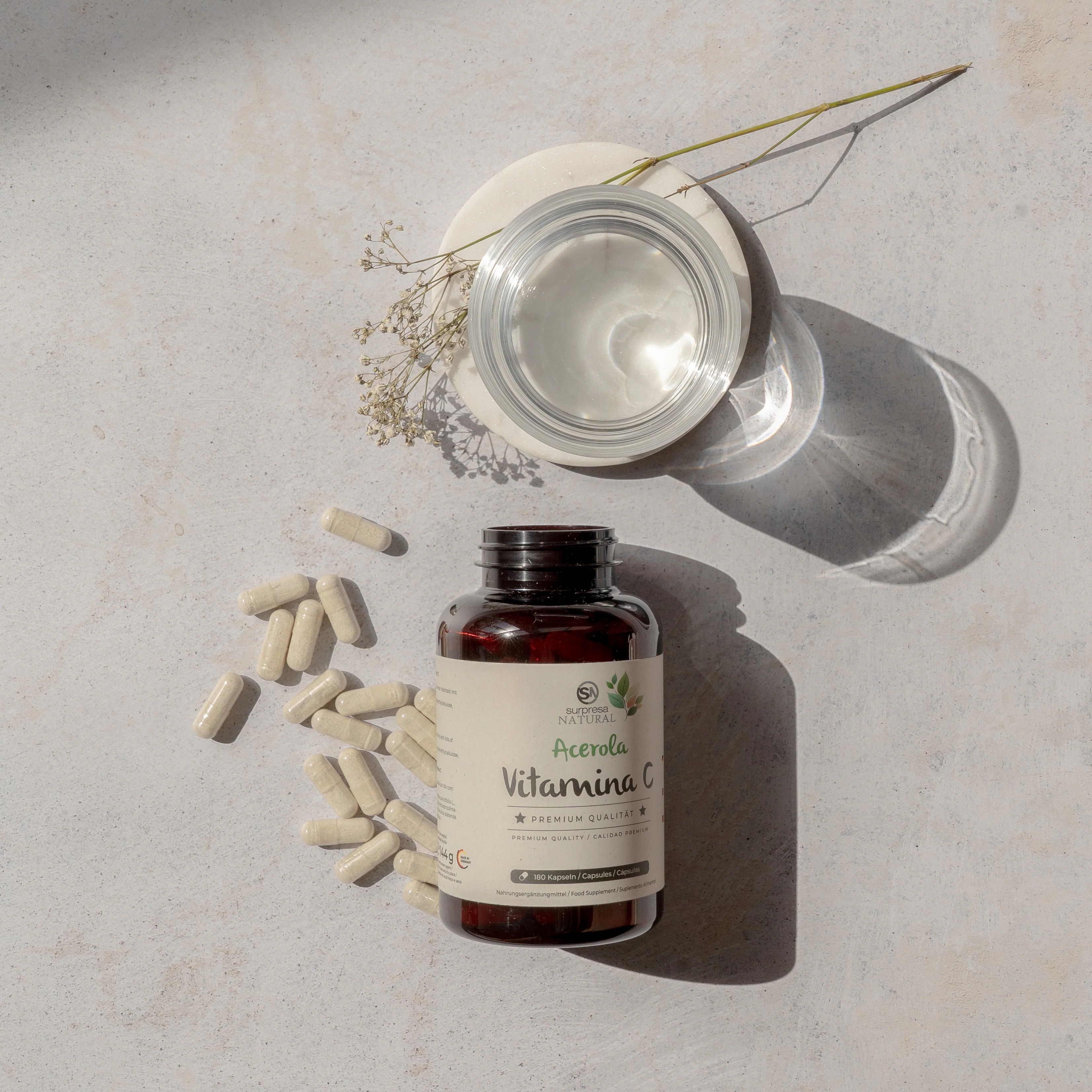 Flacone marrone con capsule e nome del prodotto. Capsule e bicchiere accanto. Su sfondo chiaro.