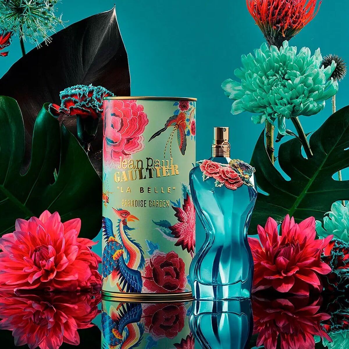 Flacone e scatola turchesi con motivi floreali. Testo: Jean Paul Gaultier La Belle Paradise Garden. Su sfondo blu.