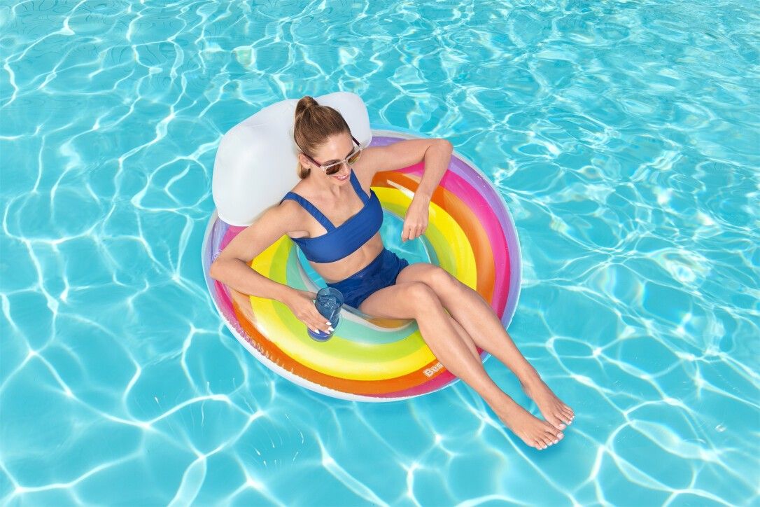 Donna seduta su un galleggiante gonfiabile arcobaleno con nuvola bianca in piscina. Marchio Bestway.